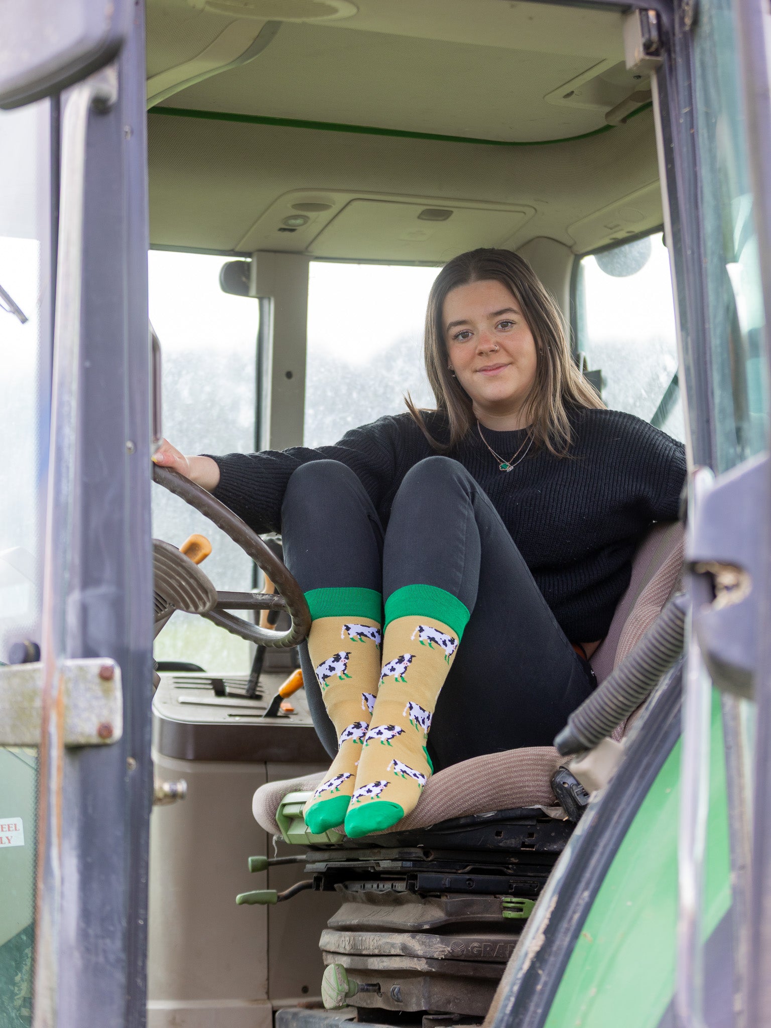 Cow socks in a crew socks style. These comfy socks have a cow design with black and white cows wearing green wellies on a mustard coloured background and a dark green top, heel and toe.