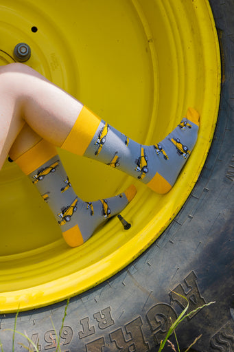 Country style combine harvester socks featuring a sleek grey background adorned with bold yellow combine harvesters, complemented by matching yellow tops, heels, and toes. These unique socks are perfect for farm, countryside and outdoor enthusiasts that adds a touch of rural flair to any wardrobe.