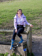 A photo of a women wearing sheep socks, crew style designed with sheep tags saying sheep 365 on a light blue background and a darker blue top, heel and toe. 
