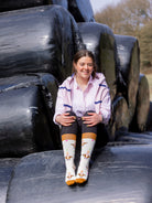 Happy Birthday cow socks. These unisex crew socks sport brown cows with party hats and green and pink stars all around, on a cream background and brown top, heel and toe. 