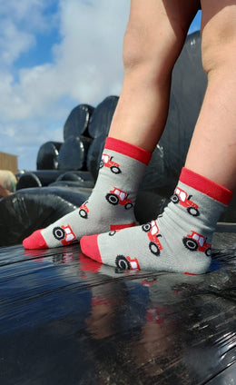 Adorable children's red tractor socks featuring playful red tractors against a stylish grey background, complete with matching red tops, heels, and toes. These fun and comfortable socks are perfect for young farm enthusiasts and add a touch of countryside charm to any outfit