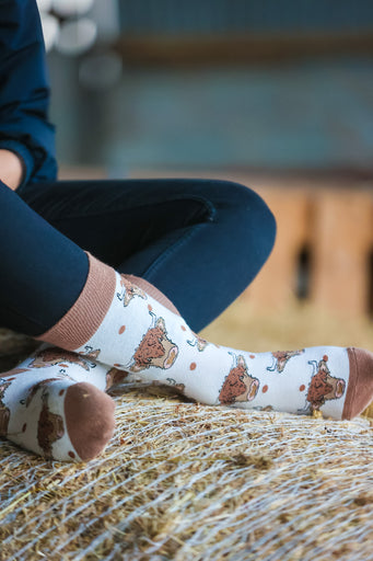 Highland cow socks set against a cream background, adorned with charming brown top heel and toe accents and playful polka dots. Featuring delightful Highland cows, these cozy socks are perfect for adding a touch to your country style wardrobe while ensuring comfort for everyday wear.