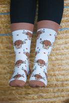 Highland cow socks set against a cream background, adorned with charming brown top heel and toe accents and playful polka dots. Featuring delightful Highland cows, these cozy socks are perfect for adding a touch to your country style wardrobe while ensuring comfort for everyday wear.