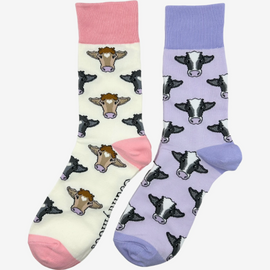 2 pairs of crew socks featuring a purple cow design on a light purple background, showcasing elegant black and brown cows with an elegant purple top, heel, and toe. Also included are pink cow socks, set against a light cream backdrop adorned with playful brown and black cows, complemented by light pink tops, heels, and toes. Perfect gifts for countryside enthusiasts, outdoor lovers and farming people, these cozy socks bring a touch of country style and comfort.