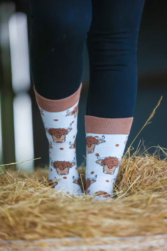 Highland cow socks set against a cream background, adorned with charming brown top heel and toe accents and playful polka dots. Featuring delightful Highland cows, these cozy socks are perfect for adding a touch to your country style wardrobe while ensuring comfort for everyday wear.