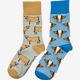 Country style blue striped socks on a white background featuring charming brown cows, paired with gracious jersey cow socks which feature light brown jersey cows on a gracious light grey background with a darker brown top heel and toe. These delightful designs capture the essence of farm life, making them perfect for outdoor enthusiasts and rural fashion lovers alike. The perfect gift to anyone who loves animals and countryside style.