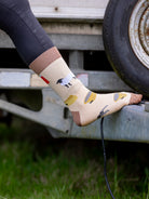 Sheep socks. A unique design with lots of sheep features all over, including a yellow sheep identification tag, grey shears, yellow bucket of feed, Suffolk sheep and a red spray can. These are all on a light peach background with a brown top, heel and toe.